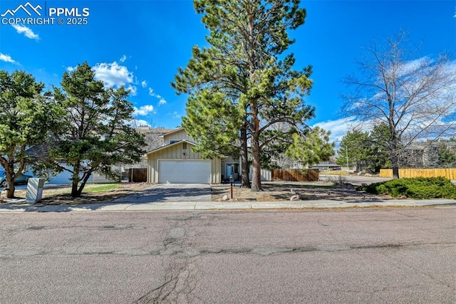 view of property hidden behind natural elements featuring board and batten siding, driveway, fence, and a garage
