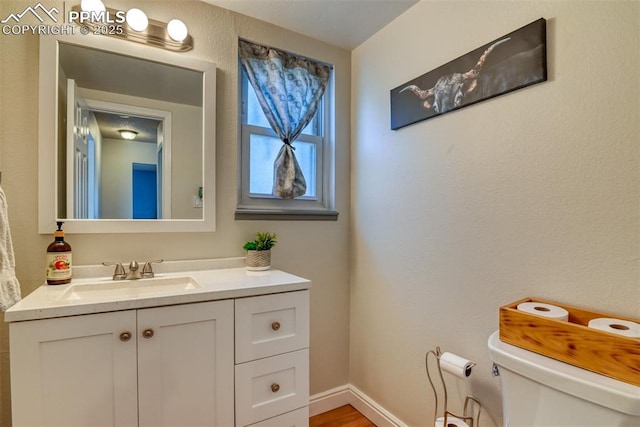 half bath with toilet, vanity, and baseboards