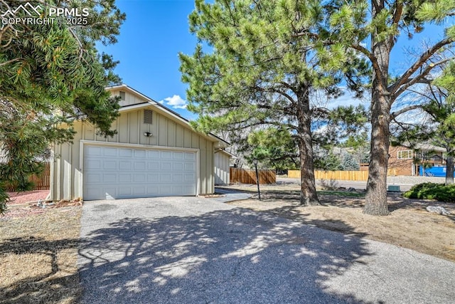 exterior space featuring board and batten siding, driveway, a garage, and fence