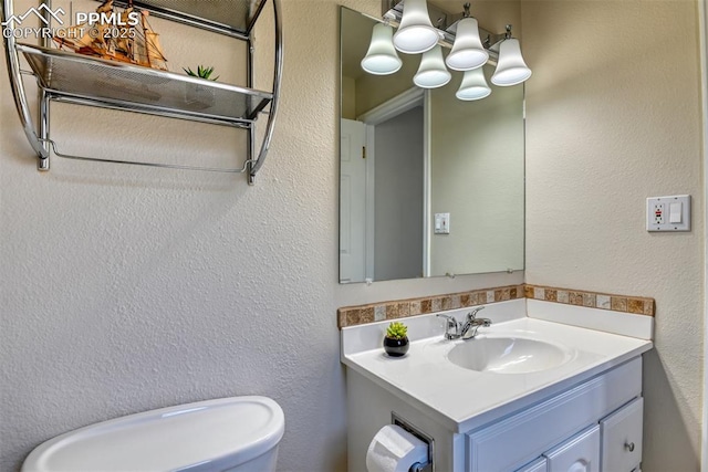 half bathroom with toilet, vanity, and a textured wall