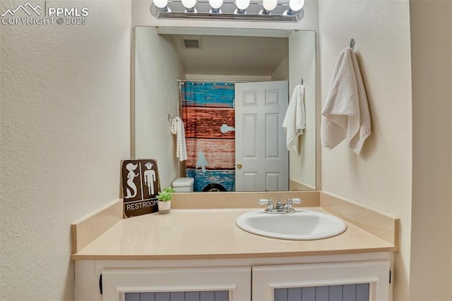 bathroom with a textured wall, visible vents, and vanity