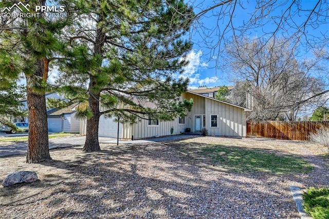 view of side of home featuring board and batten siding, driveway, a garage, and fence