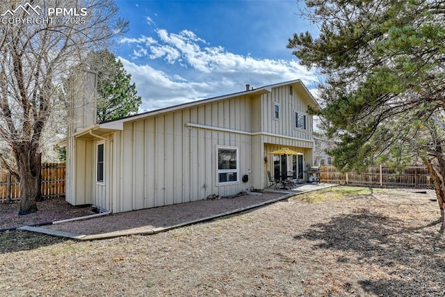 back of house featuring a fenced backyard, a chimney, a patio, and board and batten siding