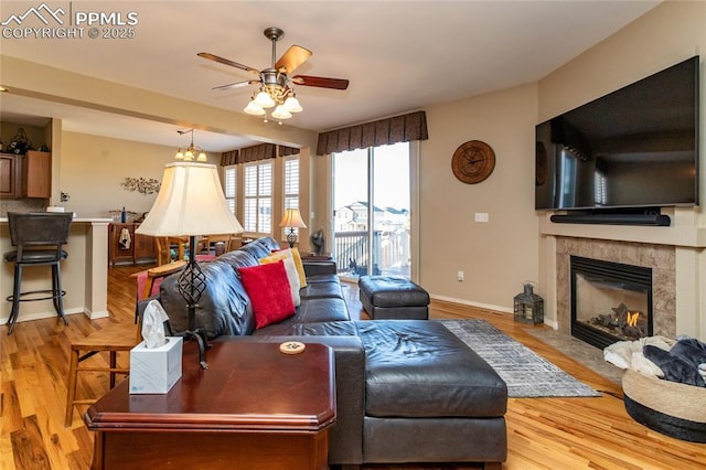 living area featuring baseboards, a ceiling fan, wood finished floors, and a fireplace