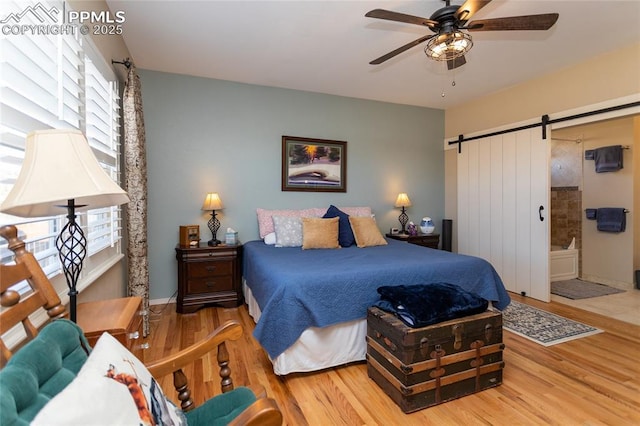 bedroom featuring ceiling fan, ensuite bathroom, a barn door, and wood finished floors