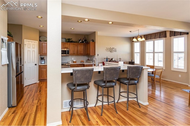 kitchen with light wood-type flooring, backsplash, appliances with stainless steel finishes, brown cabinetry, and light countertops