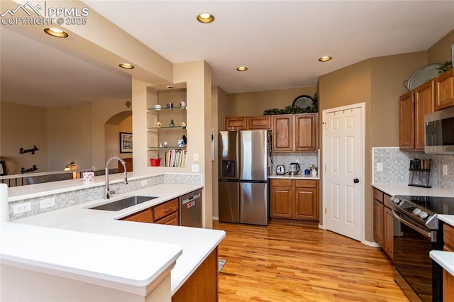 kitchen featuring brown cabinetry, a sink, light countertops, light wood-style floors, and appliances with stainless steel finishes