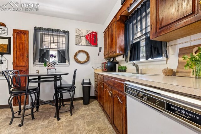 kitchen with baseboards, light countertops, decorative backsplash, white dishwasher, and a sink