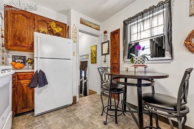 kitchen with decorative backsplash, white appliances, brown cabinetry, and light countertops