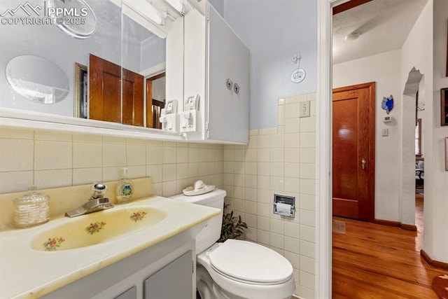 half bathroom featuring vanity, tile walls, toilet, and wood finished floors