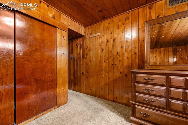 bedroom with visible vents, wood walls, carpet floors, wooden ceiling, and a closet