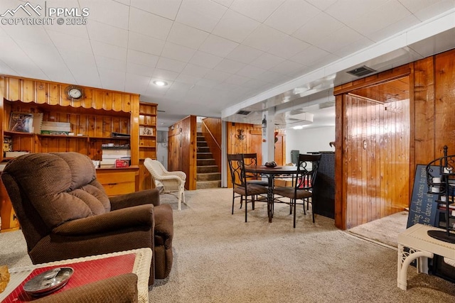 living room featuring stairway, wooden walls, and carpet