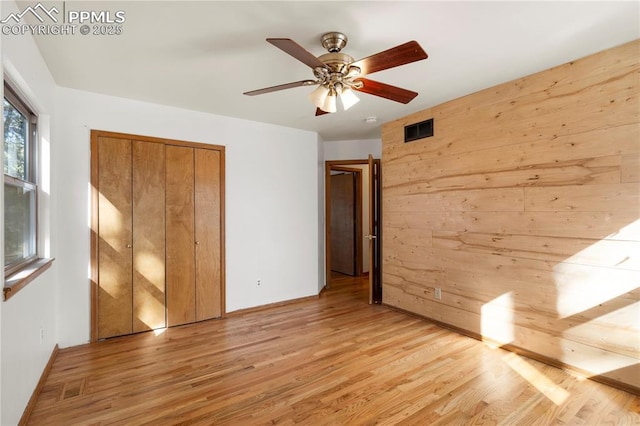 unfurnished bedroom with wooden walls, visible vents, and light wood finished floors