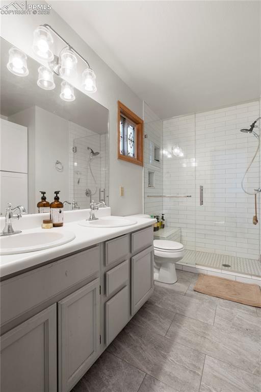 full bathroom featuring double vanity, a shower stall, toilet, and a sink