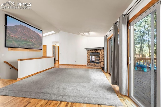 unfurnished living room with baseboards, vaulted ceiling, a stone fireplace, rail lighting, and wood finished floors