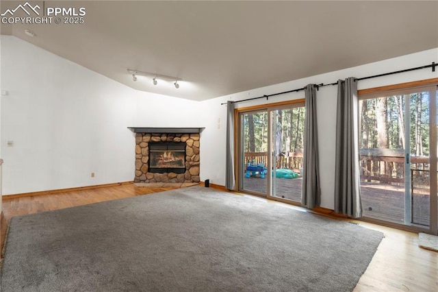 unfurnished living room featuring rail lighting, vaulted ceiling, wood finished floors, and a fireplace