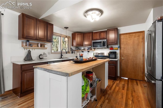 kitchen with a sink, open shelves, wood counters, wood finished floors, and stainless steel appliances