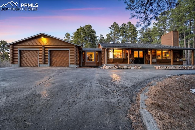 view of front of home with log siding, a garage, a chimney, and aphalt driveway