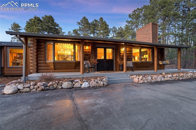 view of front of property with log siding, covered porch, and a chimney