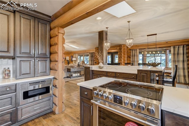 kitchen featuring light wood finished floors, built in microwave, stainless steel electric stove, decorative light fixtures, and rustic walls