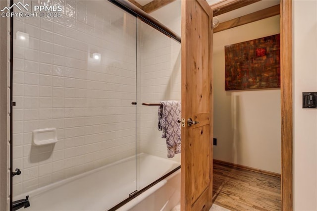 bathroom featuring enclosed tub / shower combo, baseboards, and wood finished floors