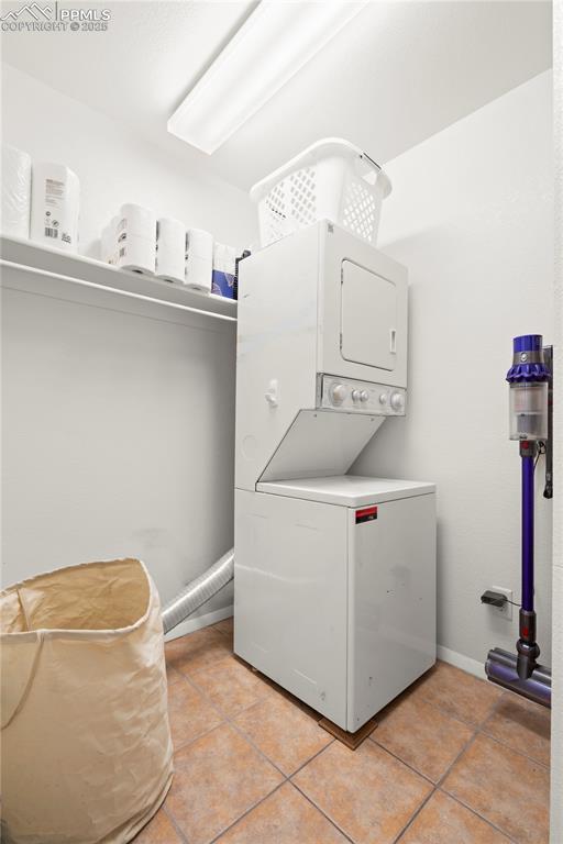 washroom featuring laundry area, light tile patterned flooring, baseboards, and stacked washing maching and dryer