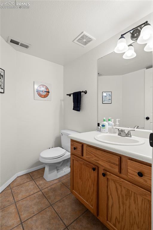 half bathroom with tile patterned flooring, visible vents, toilet, and vanity