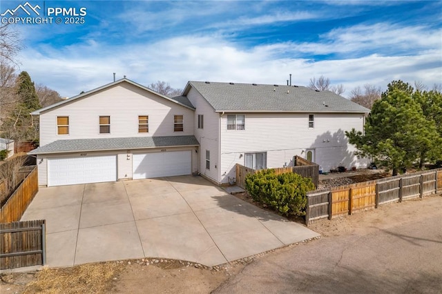 rear view of property featuring driveway, an attached garage, and fence