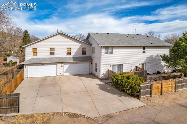 exterior space featuring concrete driveway, an attached garage, fence, and a shingled roof