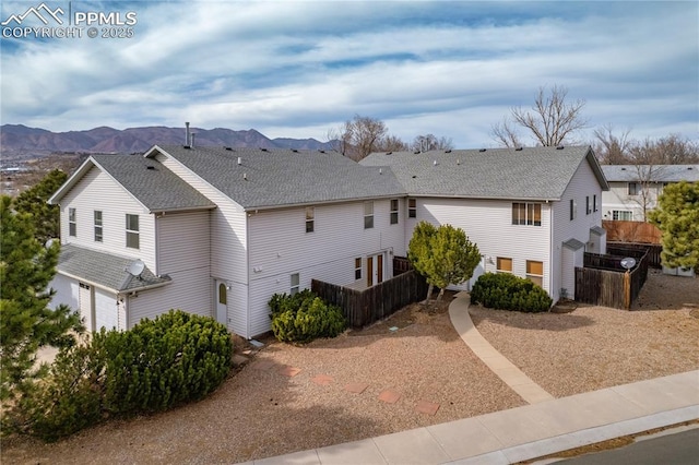 exterior space with a mountain view, a shingled roof, a garage, and fence