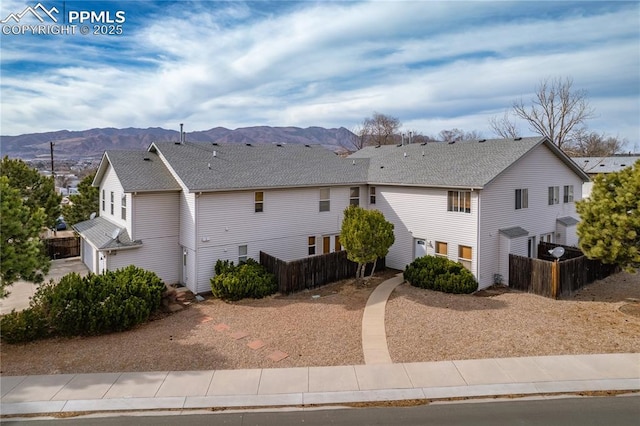 exterior space featuring a mountain view, roof with shingles, and fence