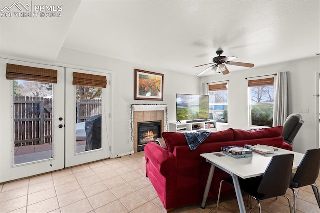 living room with ceiling fan, a tile fireplace, french doors, light tile patterned flooring, and a textured ceiling