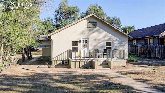 rear view of house with stucco siding, stairway, a wooden deck, and fence