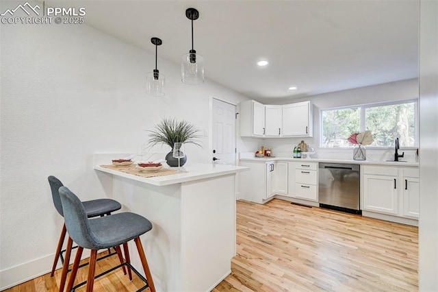 kitchen featuring light wood-type flooring, a breakfast bar, a sink, stainless steel dishwasher, and white cabinetry