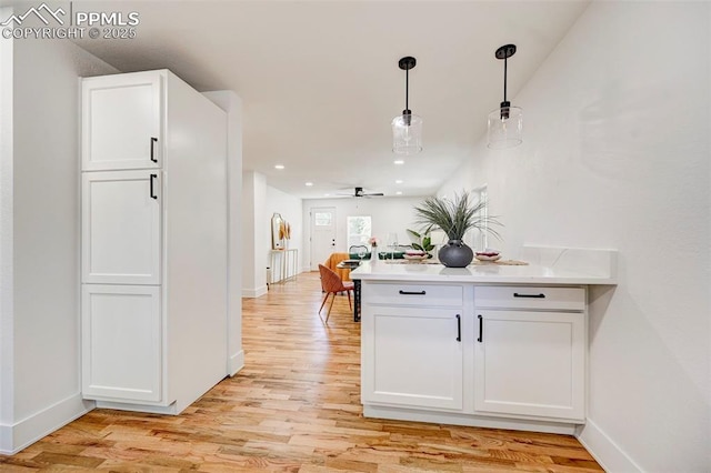 kitchen with light countertops, light wood-style flooring, a peninsula, hanging light fixtures, and white cabinetry