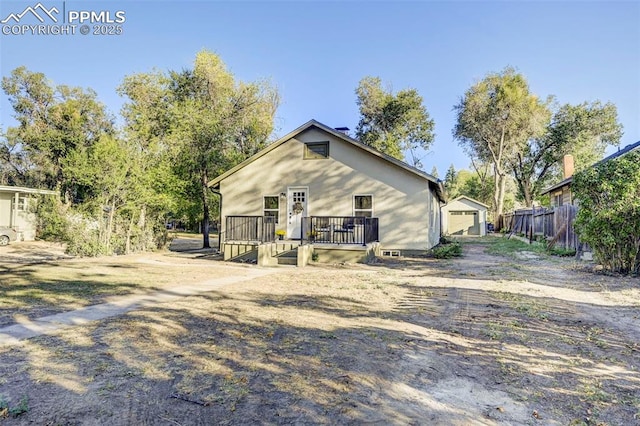 rear view of property with dirt driveway, fence, a wooden deck, an outdoor structure, and a garage