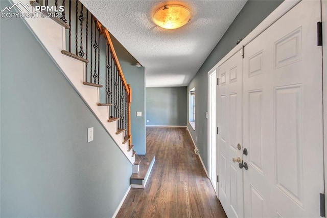 foyer featuring baseboards, stairs, a textured ceiling, and wood finished floors