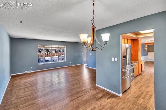 unfurnished dining area featuring a textured ceiling, visible vents, a chandelier, light wood finished floors, and baseboards
