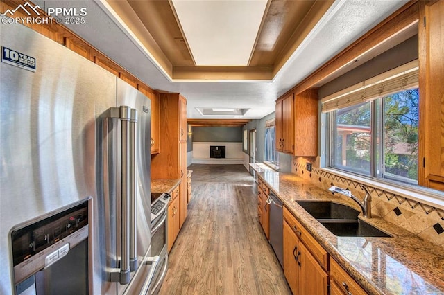 kitchen with a sink, brown cabinetry, light wood-type flooring, backsplash, and appliances with stainless steel finishes