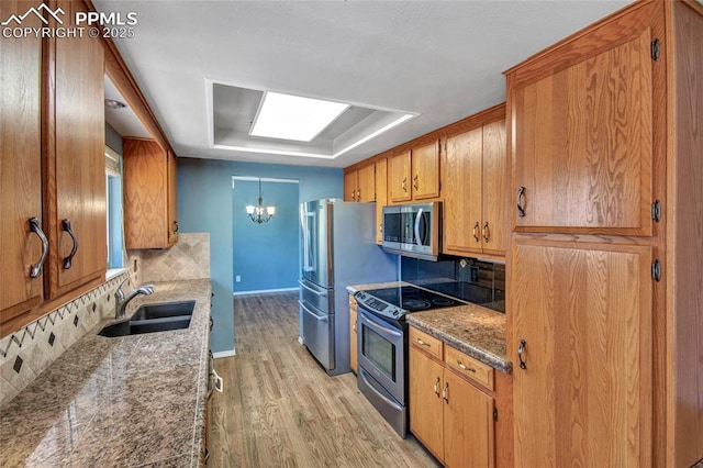 kitchen featuring a sink, a chandelier, backsplash, stainless steel appliances, and light wood-type flooring