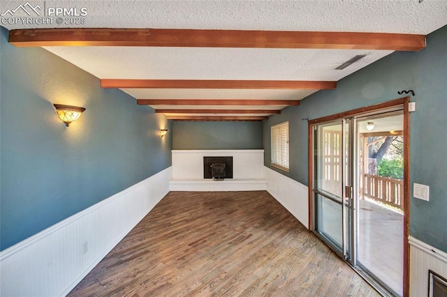 unfurnished living room with a textured ceiling, visible vents, a wainscoted wall, wood finished floors, and beamed ceiling
