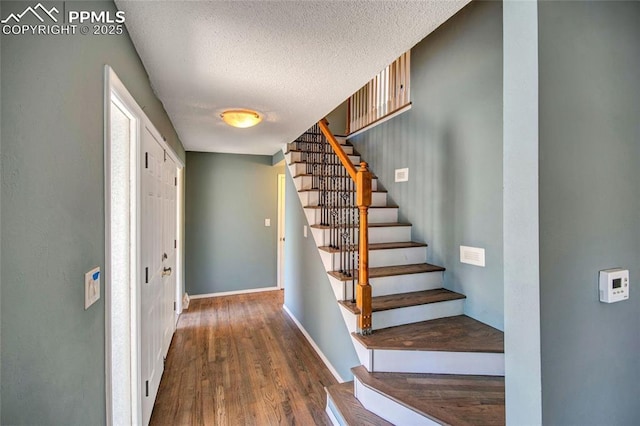 foyer entrance featuring a textured ceiling, stairway, wood finished floors, and baseboards