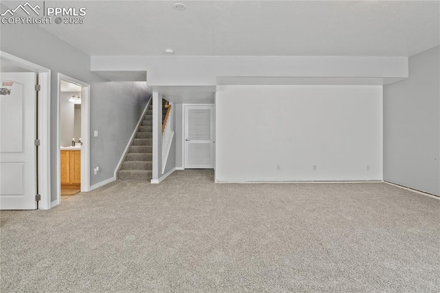 unfurnished living room featuring baseboards, light carpet, and stairway
