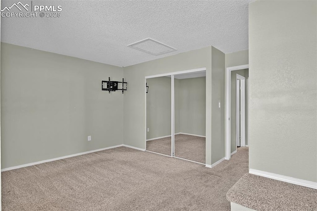 unfurnished bedroom featuring carpet, baseboards, attic access, a closet, and a textured ceiling