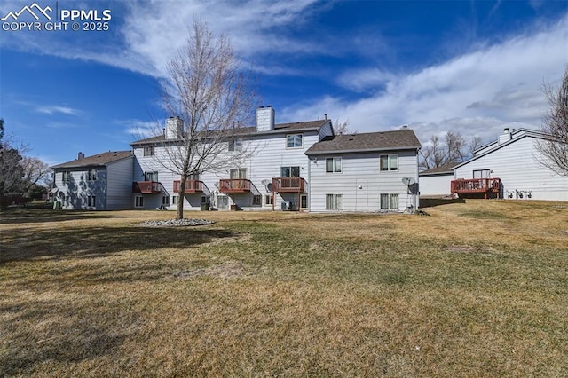 rear view of property with a wooden deck, a lawn, and a chimney
