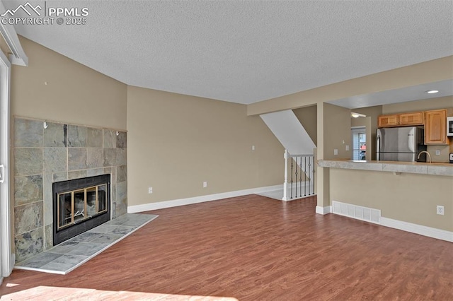unfurnished living room with a tile fireplace, wood finished floors, visible vents, and baseboards