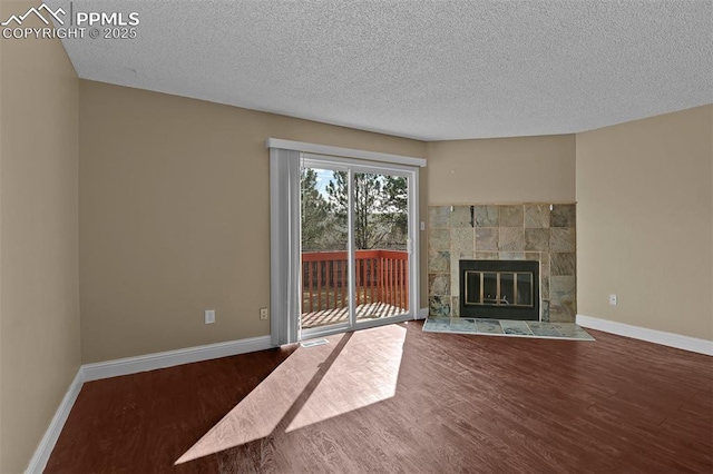 unfurnished living room with a tile fireplace, baseboards, and wood finished floors