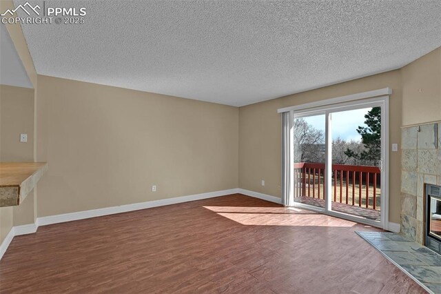 unfurnished living room with a textured ceiling, wood finished floors, baseboards, and a tile fireplace