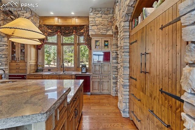 kitchen featuring light stone counters, a sink, stainless steel dishwasher, glass insert cabinets, and light wood-style floors