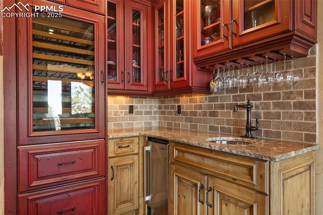 kitchen featuring glass insert cabinets, light stone counters, decorative backsplash, and a sink